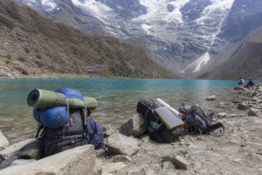 Trekkers with large packs resting beside day hikers at the Humantay Lake shoreline