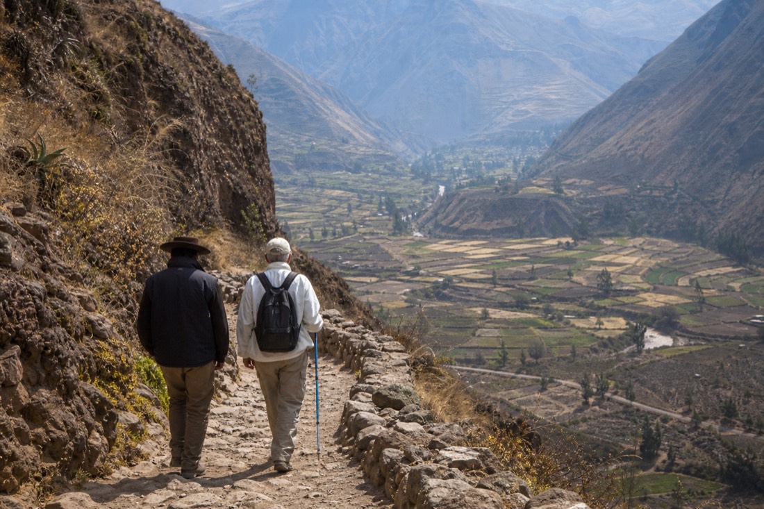 Guide walking slowly beside an older hiker on the switchbacks with the valley behind
