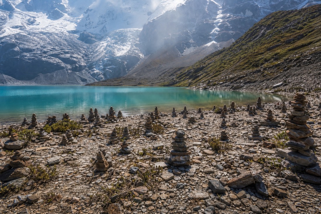 Field of small stacked stone cairns beside the turquoise water of Humantay Lake
