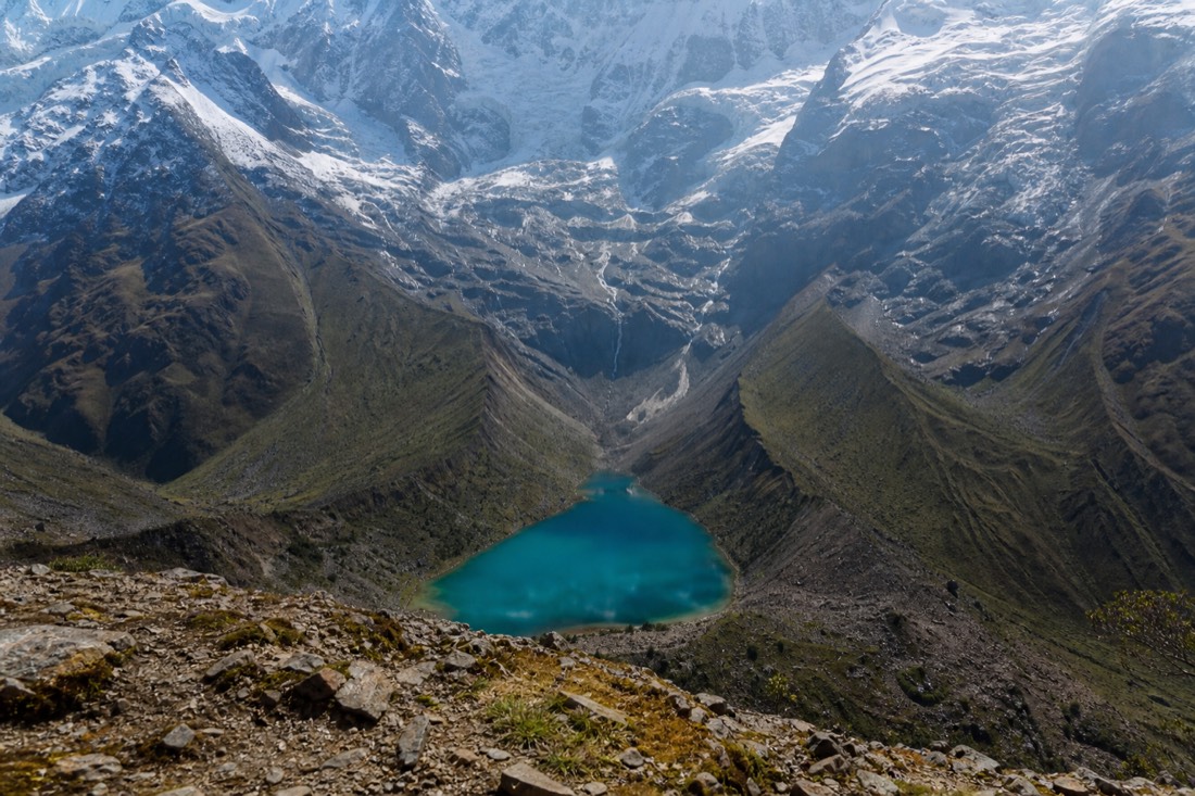 Hiker cresting the moraine lip with Humantay Lake appearing below the glacier