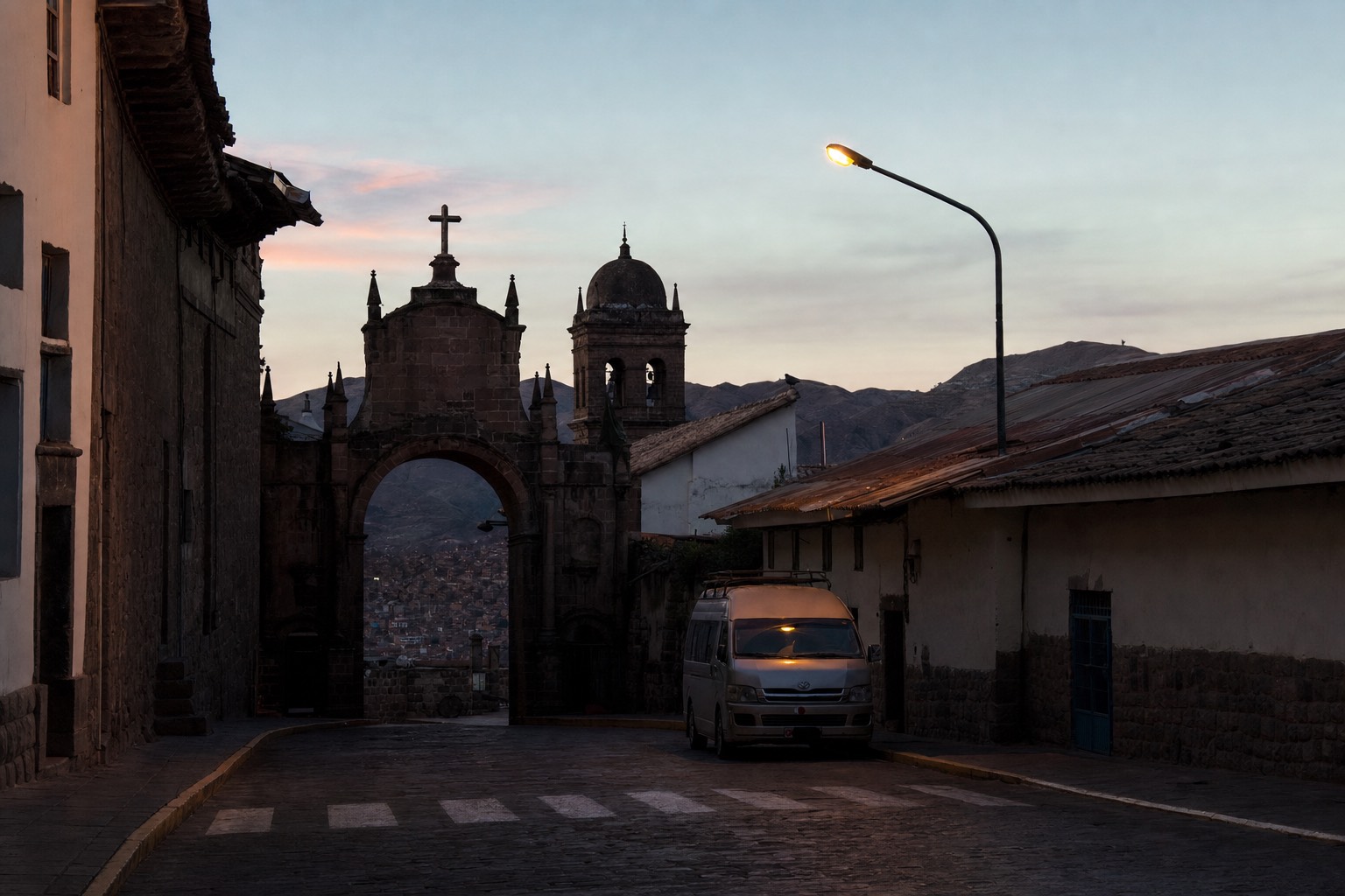 Empty pre-dawn street in Cusco's historic center with a tour van waiting under a streetlamp