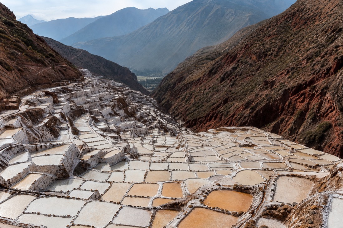 Thousands of white and copper salt evaporation ponds terraced down a hillside at Maras in low afternoon light