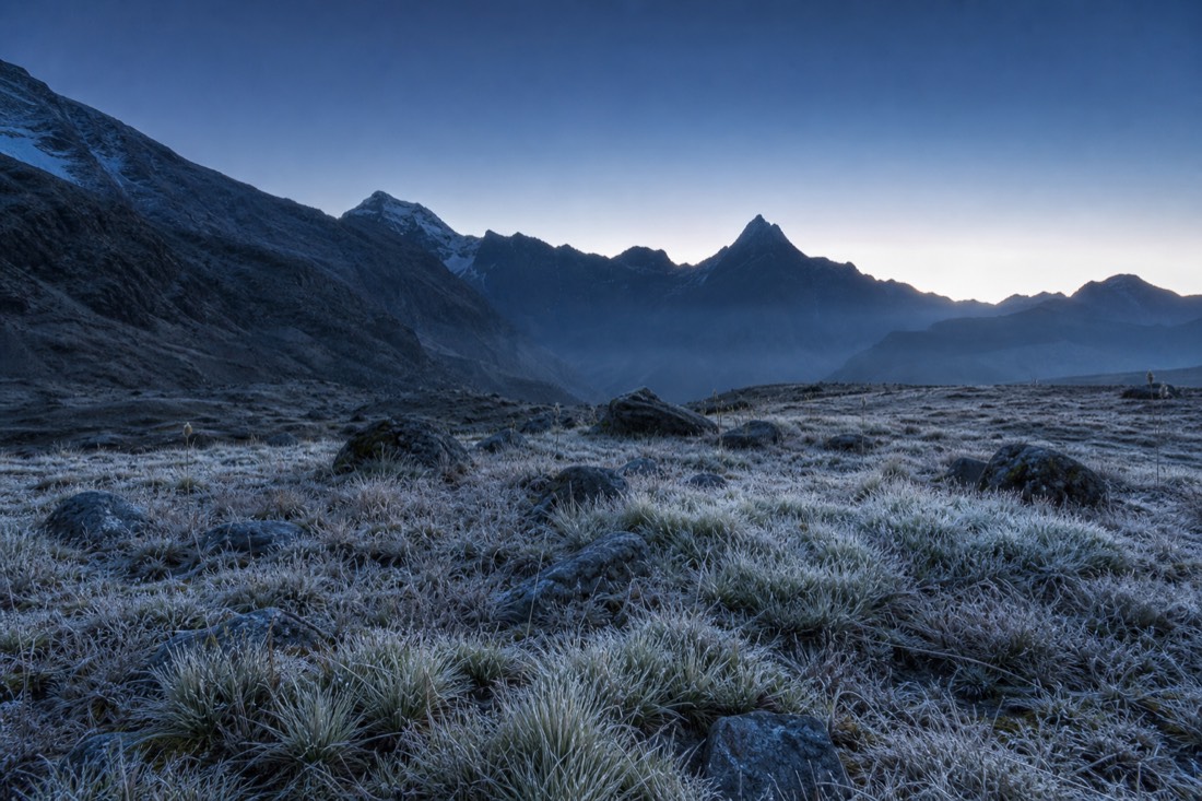 Pre-dawn frost on the high plain near Soraypampa under a deep blue sky beginning to lighten over dark mountains, no people