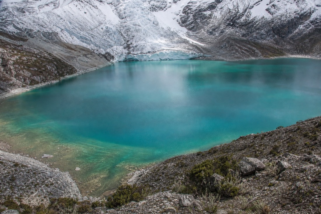 Elevated moraine viewpoint looking down over the full turquoise gradient of a glacial lake with the glacier wall behind, no people