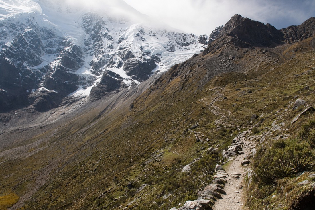 Steep rocky switchback trail climbing from the Soraypampa plain toward Humantay peak, small figures in the distance on the path