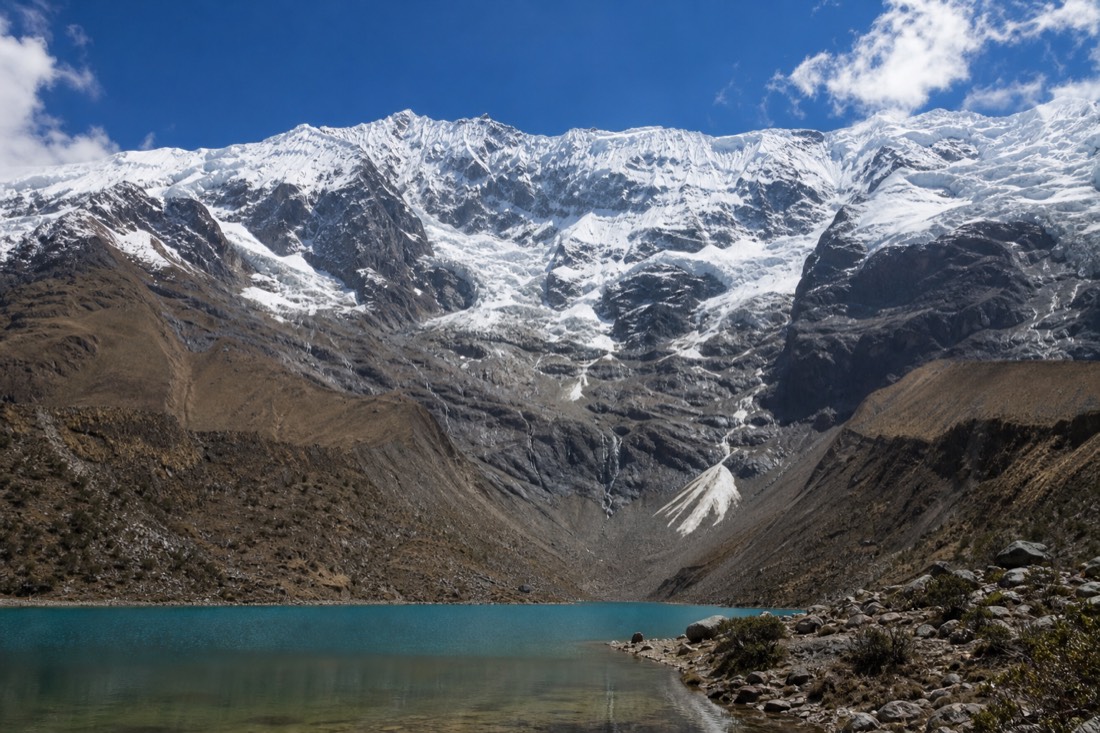 The snow and ice of Humantay peak rising steeply above the moraine and lake basin under bright high-altitude light, no people