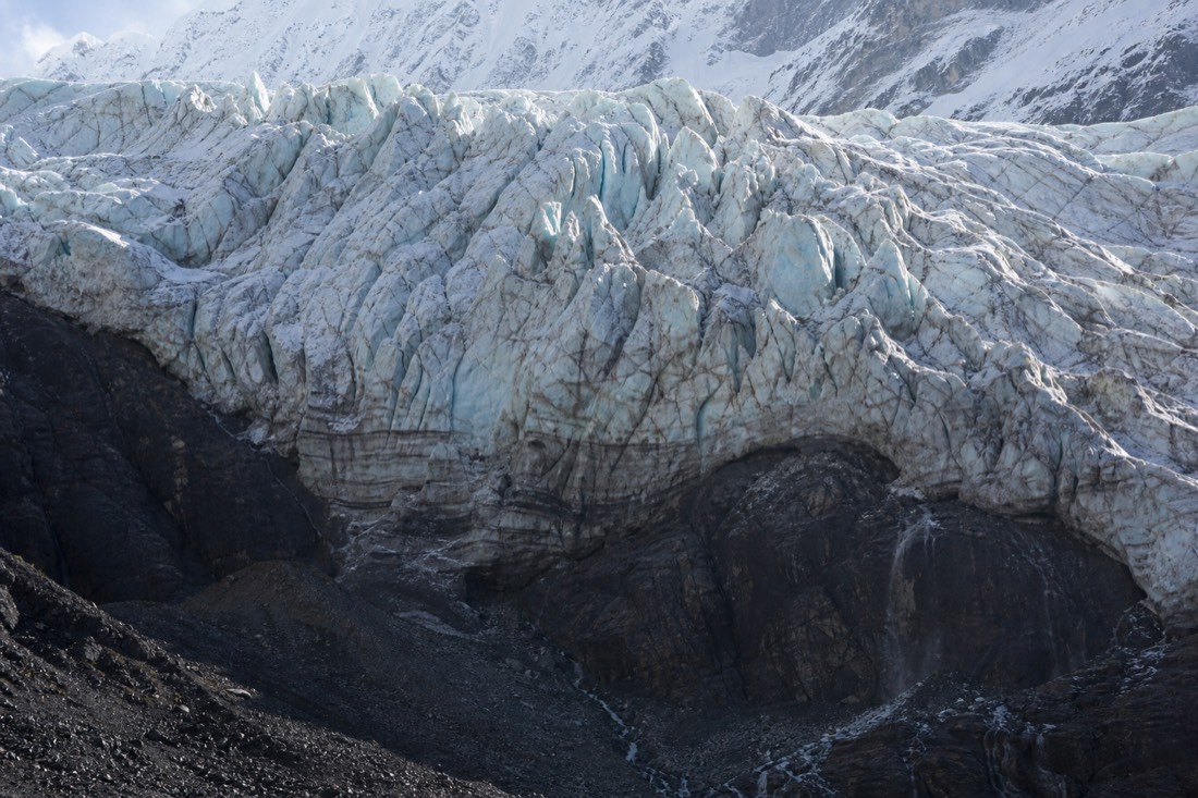 Close view of the cracked hanging glacier wall above Humantay Lake with dark moraine rock below in morning light, no people