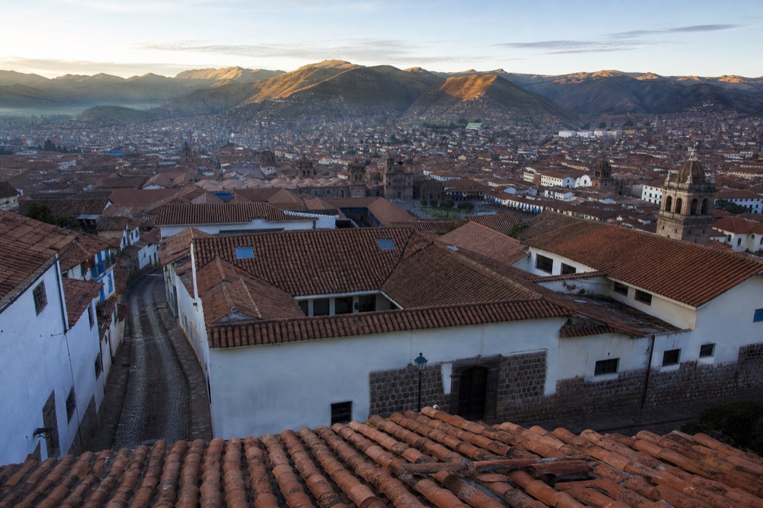 Terracotta rooftops of Cusco at dawn with Andean peaks on the horizon and a quiet empty street