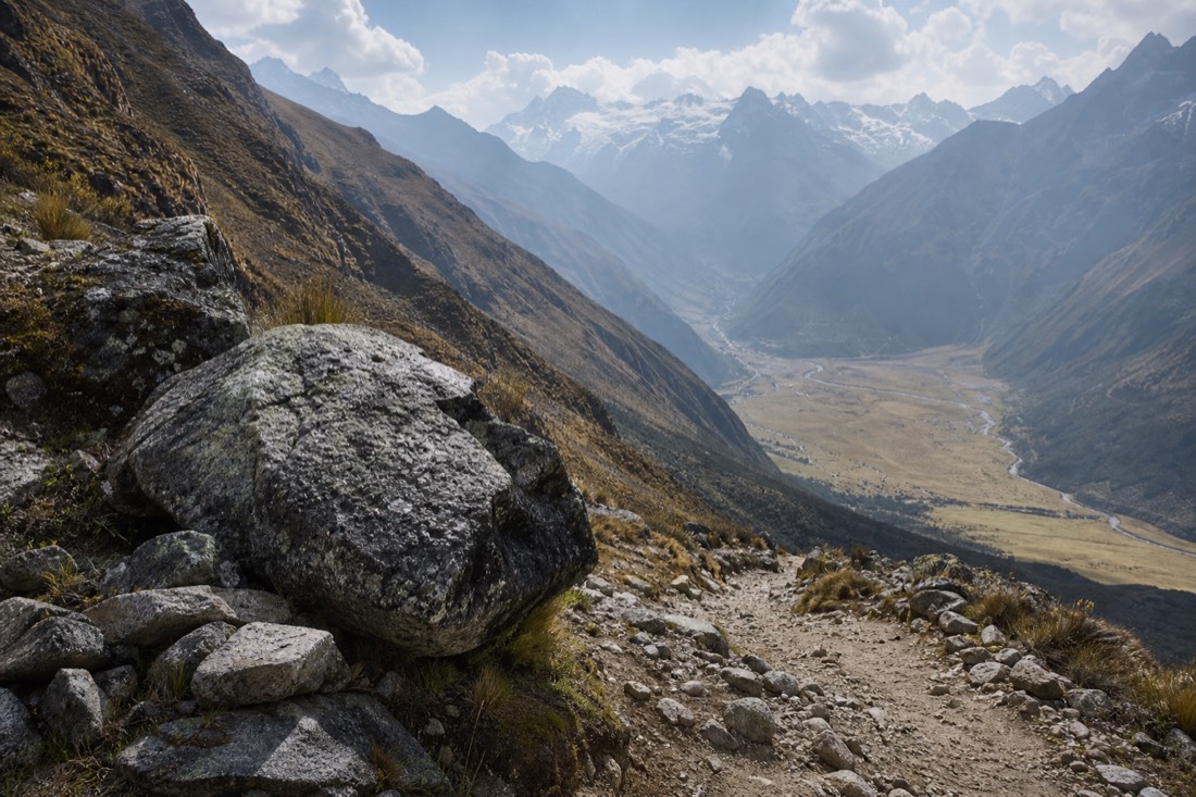 A natural rest point of large boulders beside the Humantay trail with the Soraypampa plain far below, empty trail