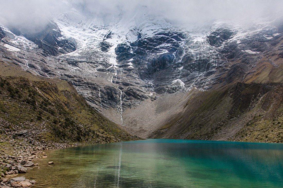 Glacial meltwater streaming into the turquoise Humantay Lake from the ice field above, fine rock sediment clouding the shallows
