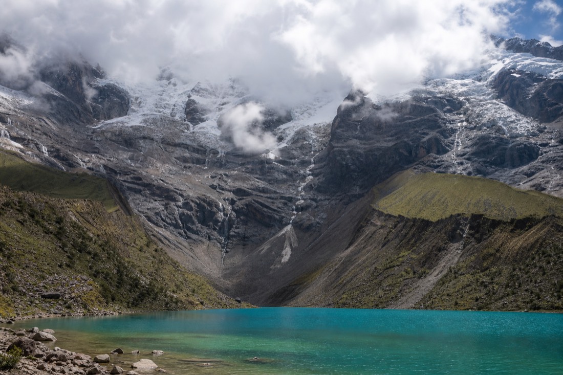 Cloud building over the Humantay glacier above a rocky moraine, mid-morning light on the turquoise lake below