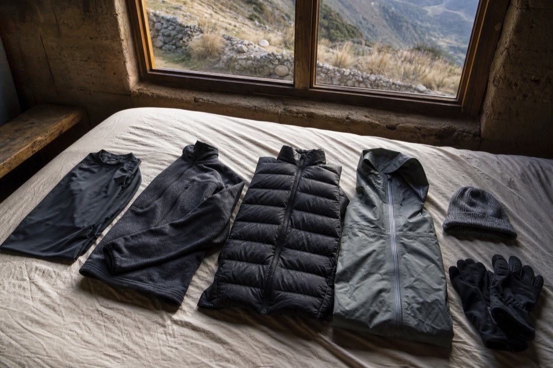 Hiking layers laid out on a bed the night before a Humantay trip: base layer, fleece, packable down jacket, rain shell, hat and gloves, no text, no faces