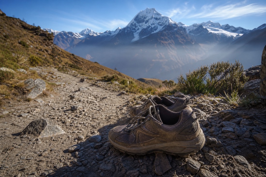 Well-worn trail shoes on a rocky dusty Andean path near Soraypampa, loose stones and alpine grass around them, no people, no text