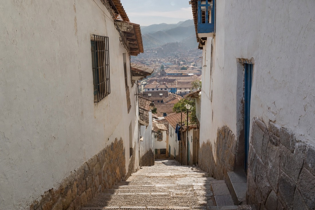 Narrow whitewashed cobbled lane in Cusco's historic centre in the evening, stone steps climbing between colonial walls