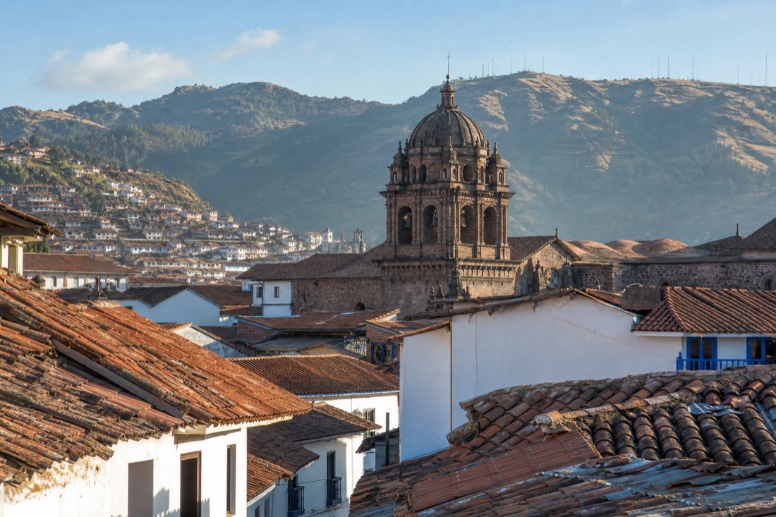Terracotta rooftops of the San Blas neighbourhood in Cusco at morning light, church tower and green hills behind
