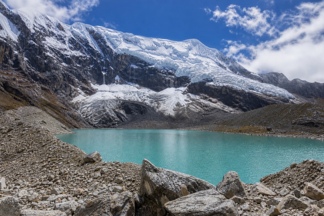 Wide view of Humantay Lake with the glacier face above and stone cairns along the shore